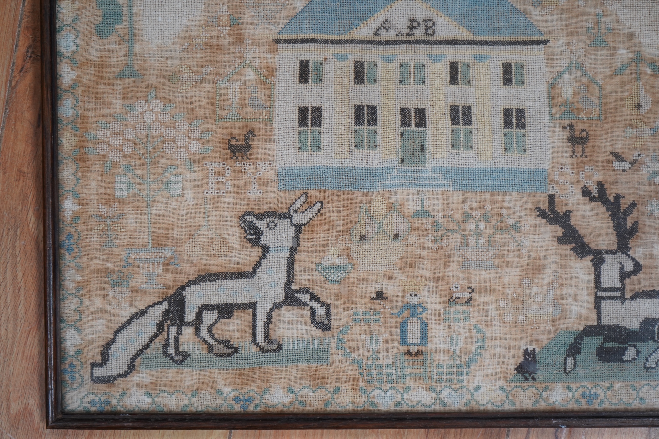 A framed 18th century sampler, dated 1779 by SS., worked in fine cross stitch with motifs of angels, figures, flowers, trees birds a fox and a stag surrounding a house with initials APB. 39cm x 37.5cm. Condition - the em